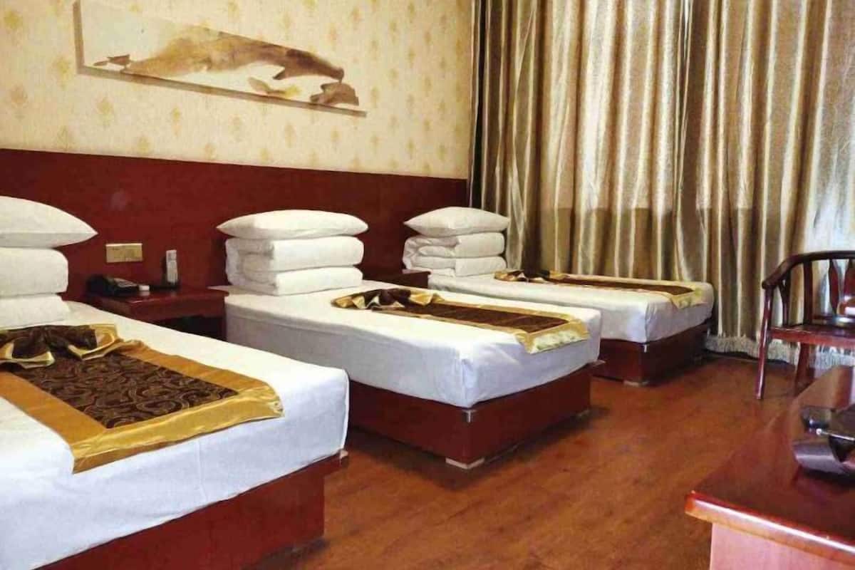A hotel room with three single beds, a desk, a chair, and a curtain.