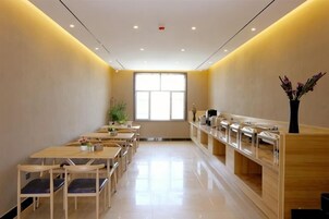 Un comedor de hotel con varias mesas y sillas, una recepción y un amplio ventanal que proporciona luz natural.