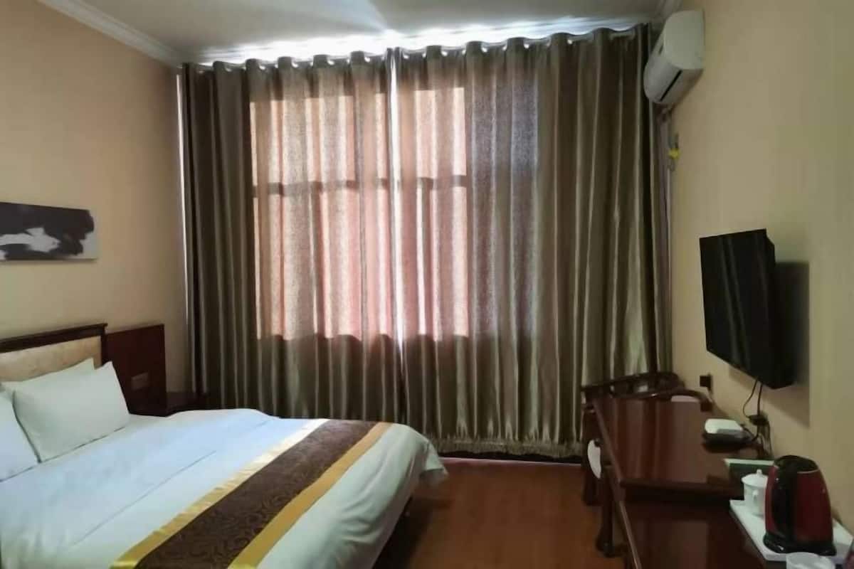 A hotel room with a bed, a desk, a chair, a television, and curtains.
