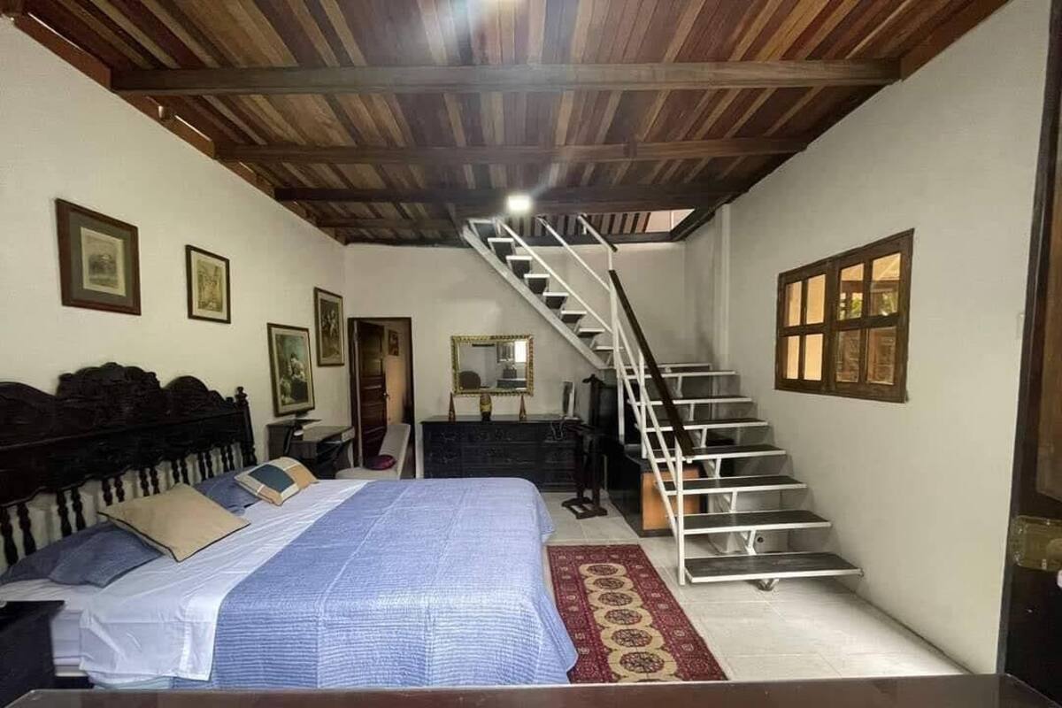 Un dormitori amb un llit, un panell de capçal de fusta, una escala i un mirall.