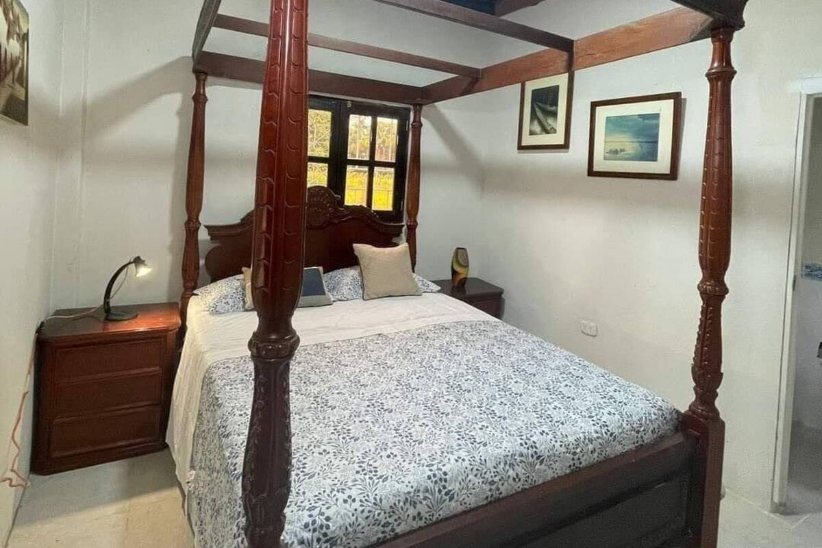 Un llit amb cortines que formen dos pilars en una habitació amb sostre inclinat i bigues de fusta.