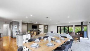 Una cocina moderna con una isla central, comedor con una mesa de madera dispuesta para seis personas y una sala de estar con chimenea.