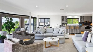 Una sala de estar moderna con un sofá gris, una mesa de centro blanca y una cocina al fondo.