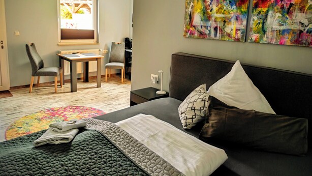 Un dormitorio moderno con una cama, un escritorio y dos sillas. Hay pinturas abstractas en la pared.
