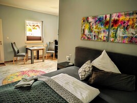 Quarto moderno com cama, escrivaninha e duas cadeiras. Há quadros abstratos na parede.