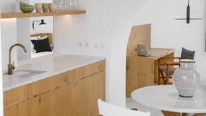 Une cuisine moderne avec des meubles en bois, un plan de travail blanc et une table de salle à manger ronde agrémentée d’un vase à rayures.