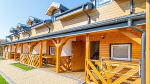 Een rij houten vakantiehuisjes, elk met een bijbehorend terras, een raam en een deur.