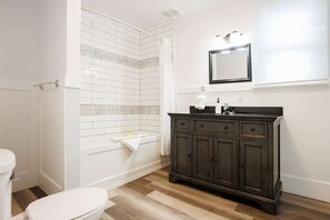 A bathroom with a white toilet, a shower, a bathtub, and a dark wooden vanity with a mirror above the sink. - 86B  King Bed - Downtown - Walk everywhere (Charlottetown)