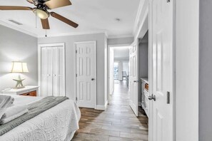 A bedroom with a bed, a ceiling fan, a nightstand with a lamp, and a hallway leading to other rooms.