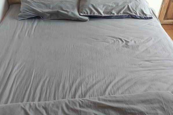 A bed with a grey sheet and two pillows.