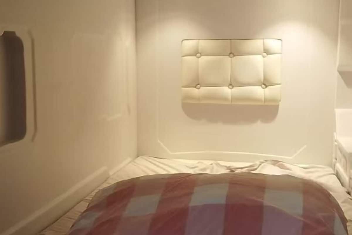 Un dormitori amb un capçal tapissat, un llit amb coixí escocès i una paret blanca.