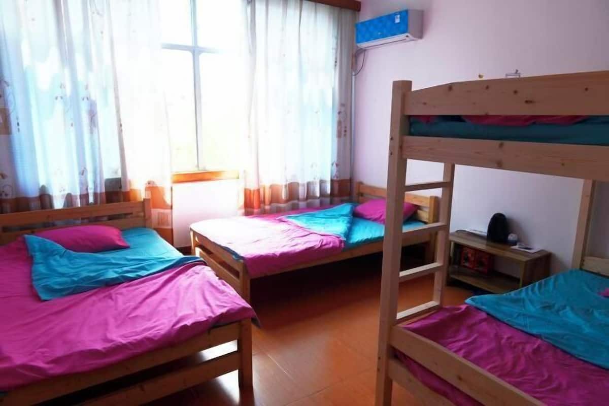 Una habitació de dormitori amb lliteres, una finestra amb cortines, un radiador fixat a la paret i una taula de nit petita.