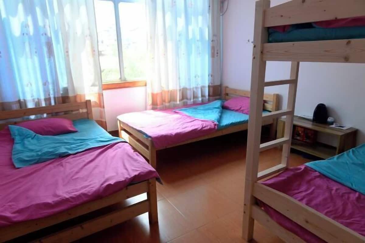 Dormitori amb lliteres, una finestra amb cortines lleugeres i una escala de fusta.