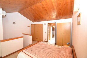 A bedroom with a wooden ceiling, a bed with patterned bedding, and wooden wardrobes.