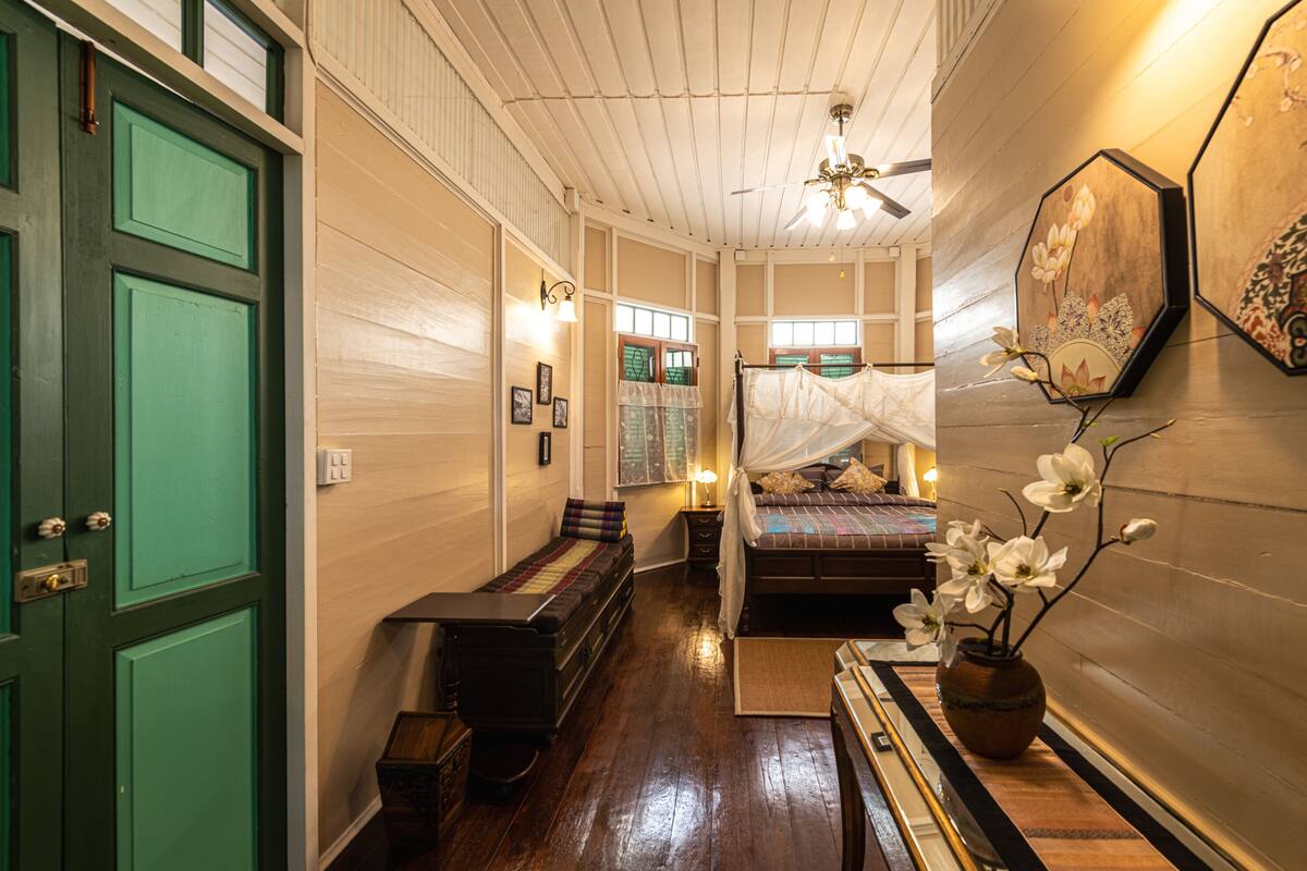 Quarto tradicional com cama, um banquinho e uma pequena mesa.
