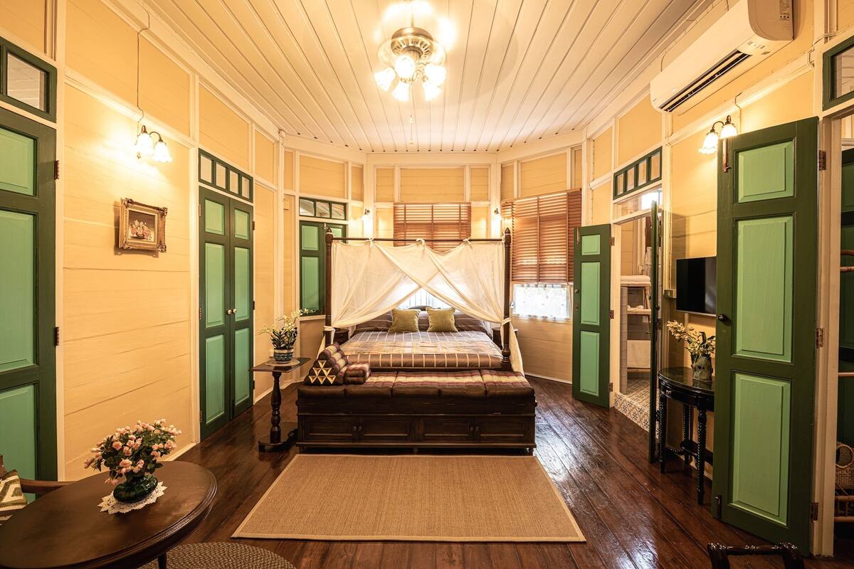 Quarto com cama de dossel, piso de madeira e portas verdes.