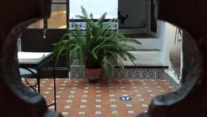 Uitzicht door een ronde opening van een kamer met betegelde vloer, een potplant en een bed met een gestreept hoofdeinde.