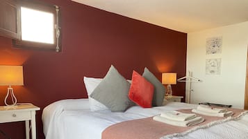 Una cama bien hecha con almohadas, una mesita de noche con una lámpara y un perchero con toallas.