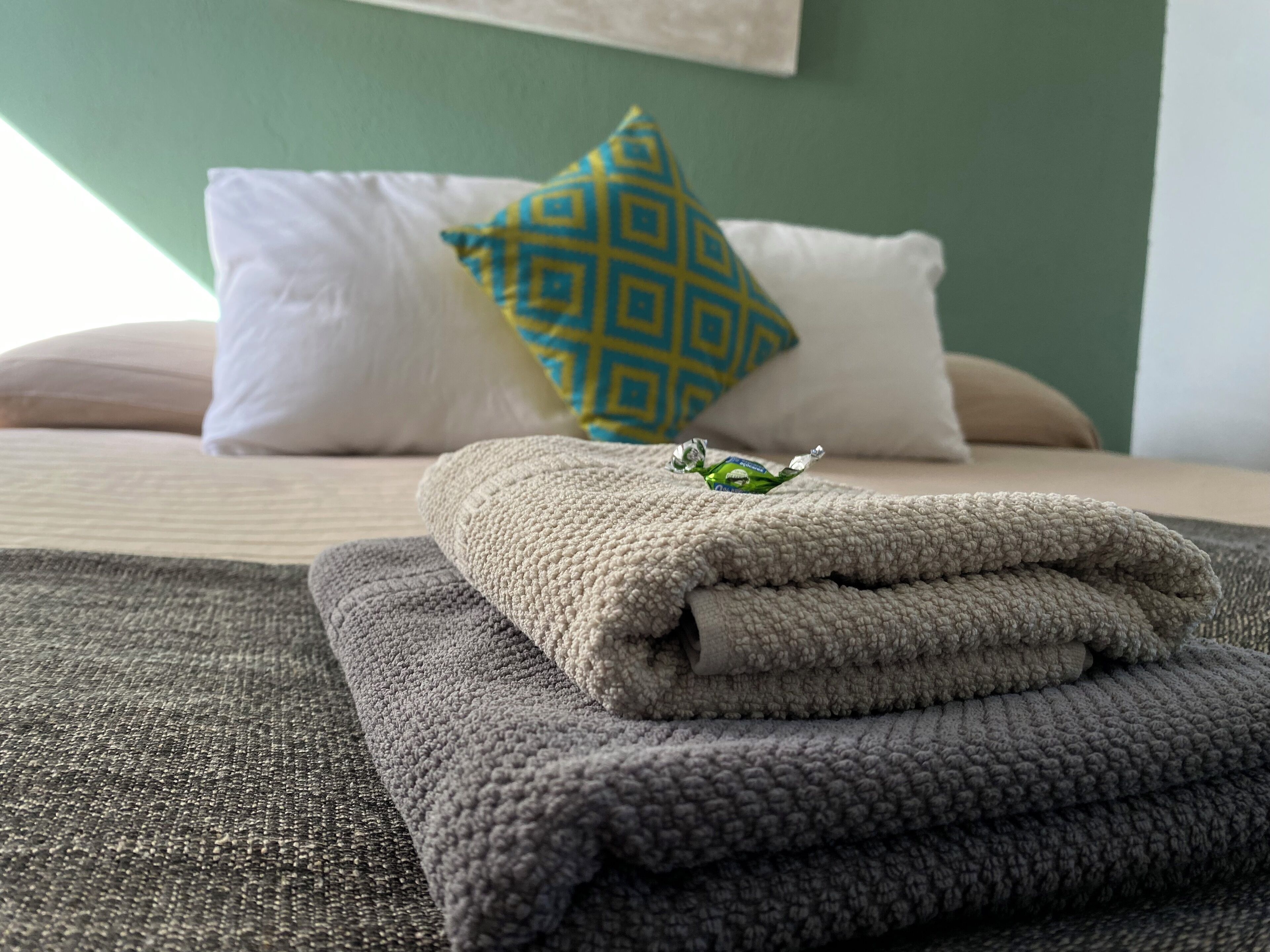 A neatly made bed with folded towels, a decorative pillow, and a small item on the bed.