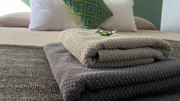 A neatly made bed with folded towels, a decorative pillow, and a small item on the bed.