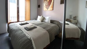 Een slaapkamer met een bed, een raam, een schilderij en een spiegel.