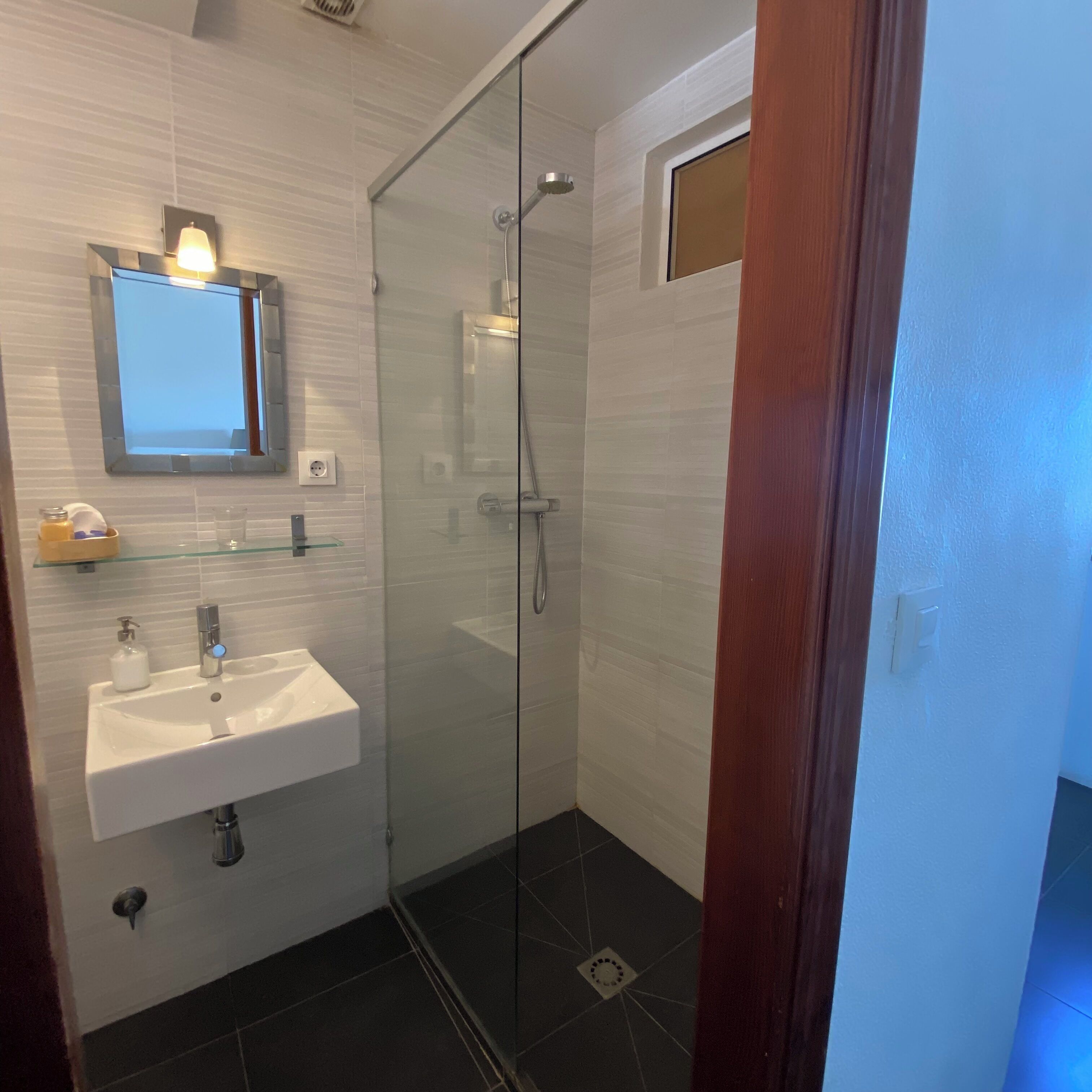 Een moderne badkamer met een douchecabine van glas, een witte wastafel en een spiegel erboven.