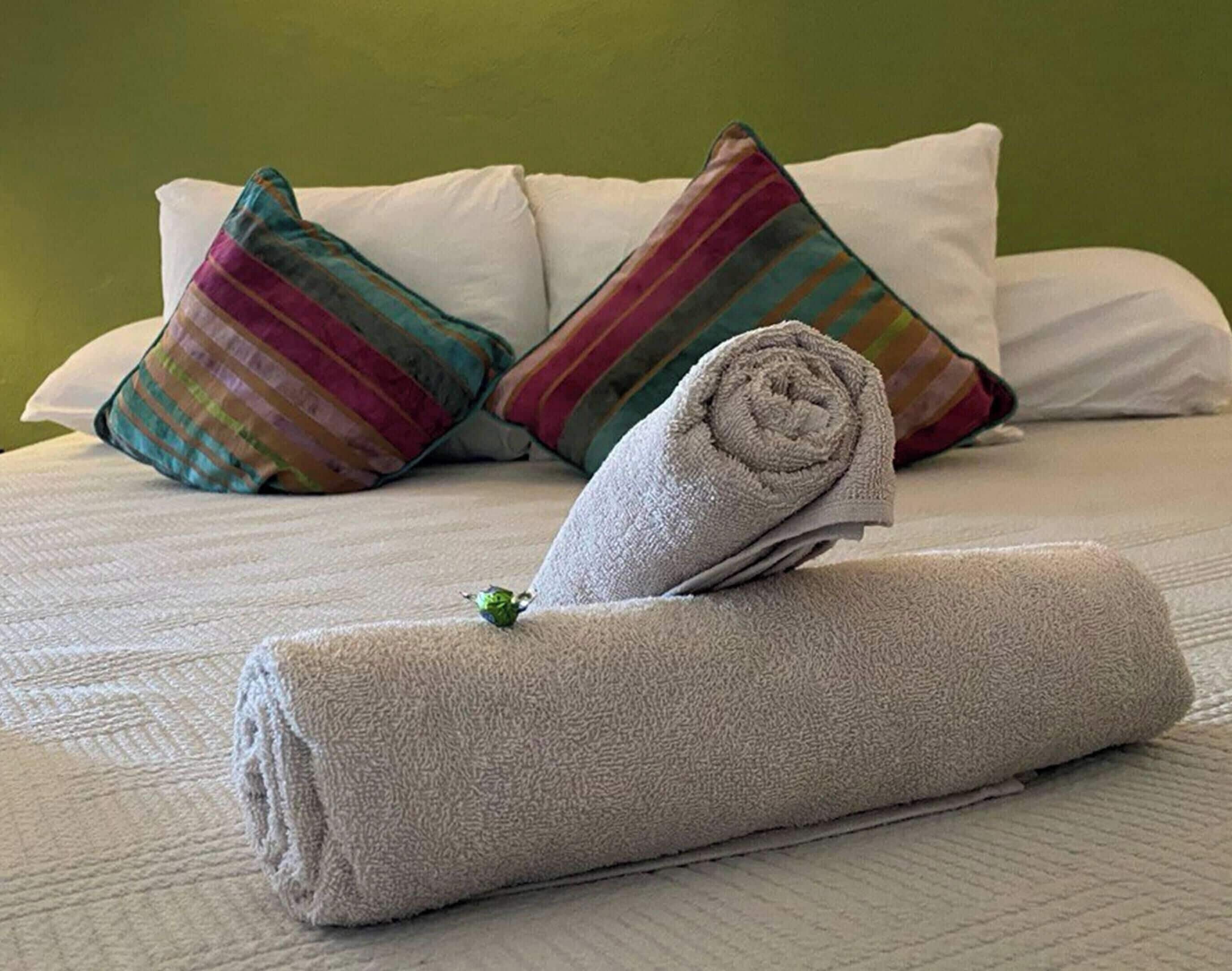 A neatly made bed with white linens, a rolled towel, and colorful striped pillows.