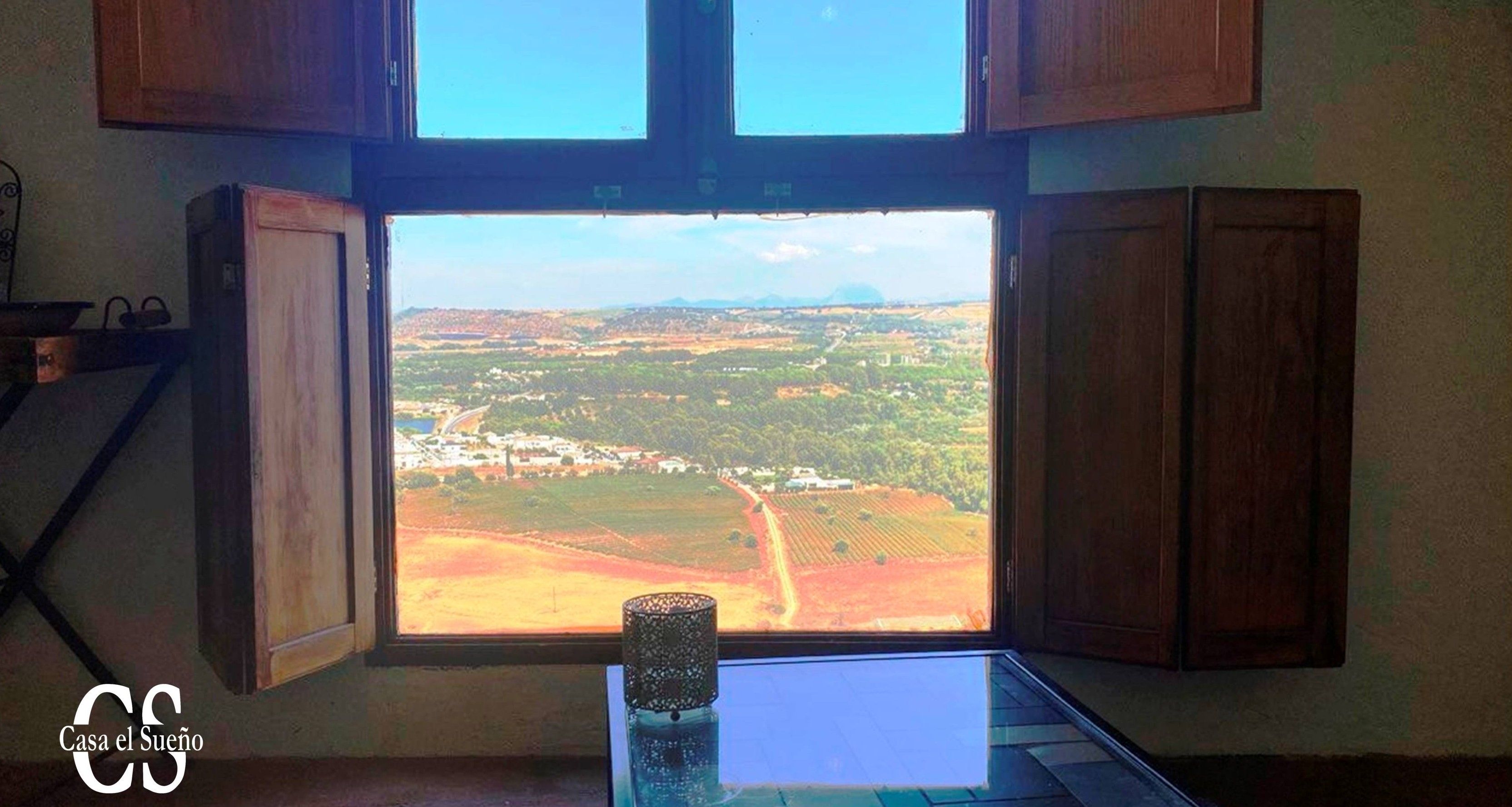 A room with a large window offering a view of a rural landscape.