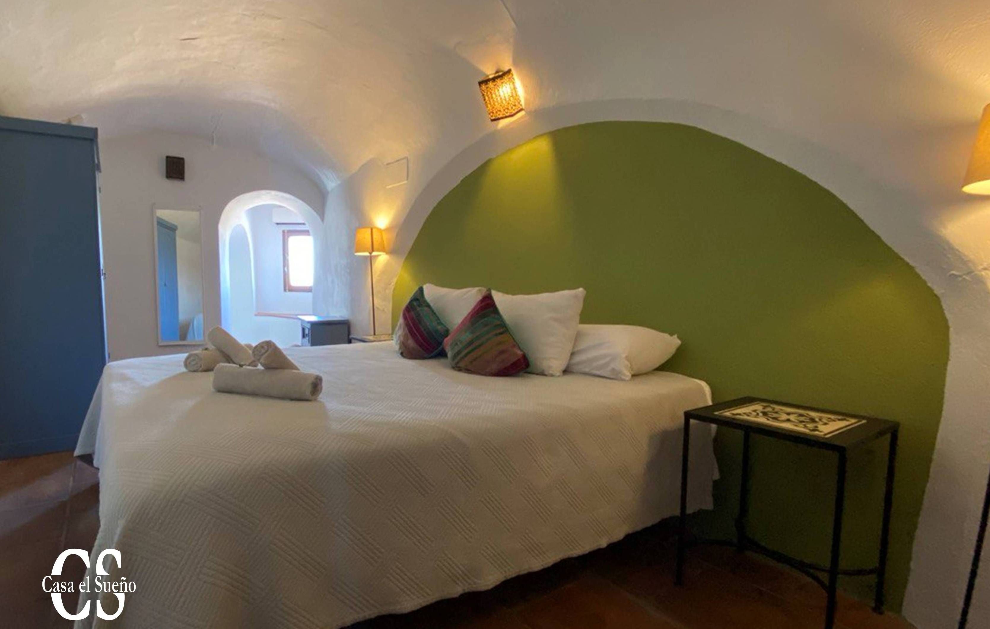 Un dormitorio con cama, almohadas, mesita de noche y lámpara.