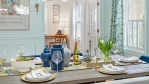 Un comedor con una mesa dispuesta para cuatro, destacando jarrones de cerámica azul y blanco, copas de vino y un jarrón con tulipanes.