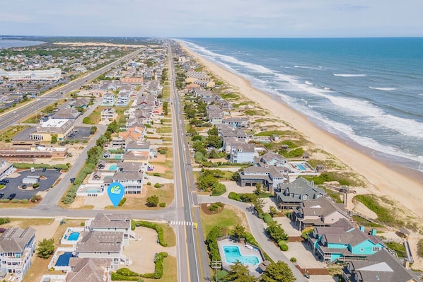 An aerial view of a coastal residential area with houses, a beach, and a road.