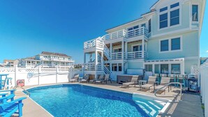 A swimming pool with lounge chairs and a multi-story building with balconies. - Aqua Palooza 🌊 Semi-Oceanfront 🏖️Pool & Hot Tub 💦 Elevator ⬆️ Pet Friendly🐕 (Nags Head)