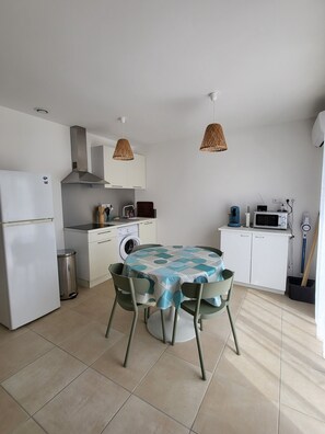 A compact kitchen with a refrigerator, washing machine, microwave, and a dining table with chairs. - Spacious and cosy T3 - walking distance to the beach - swimming pool (Linguizzetta)