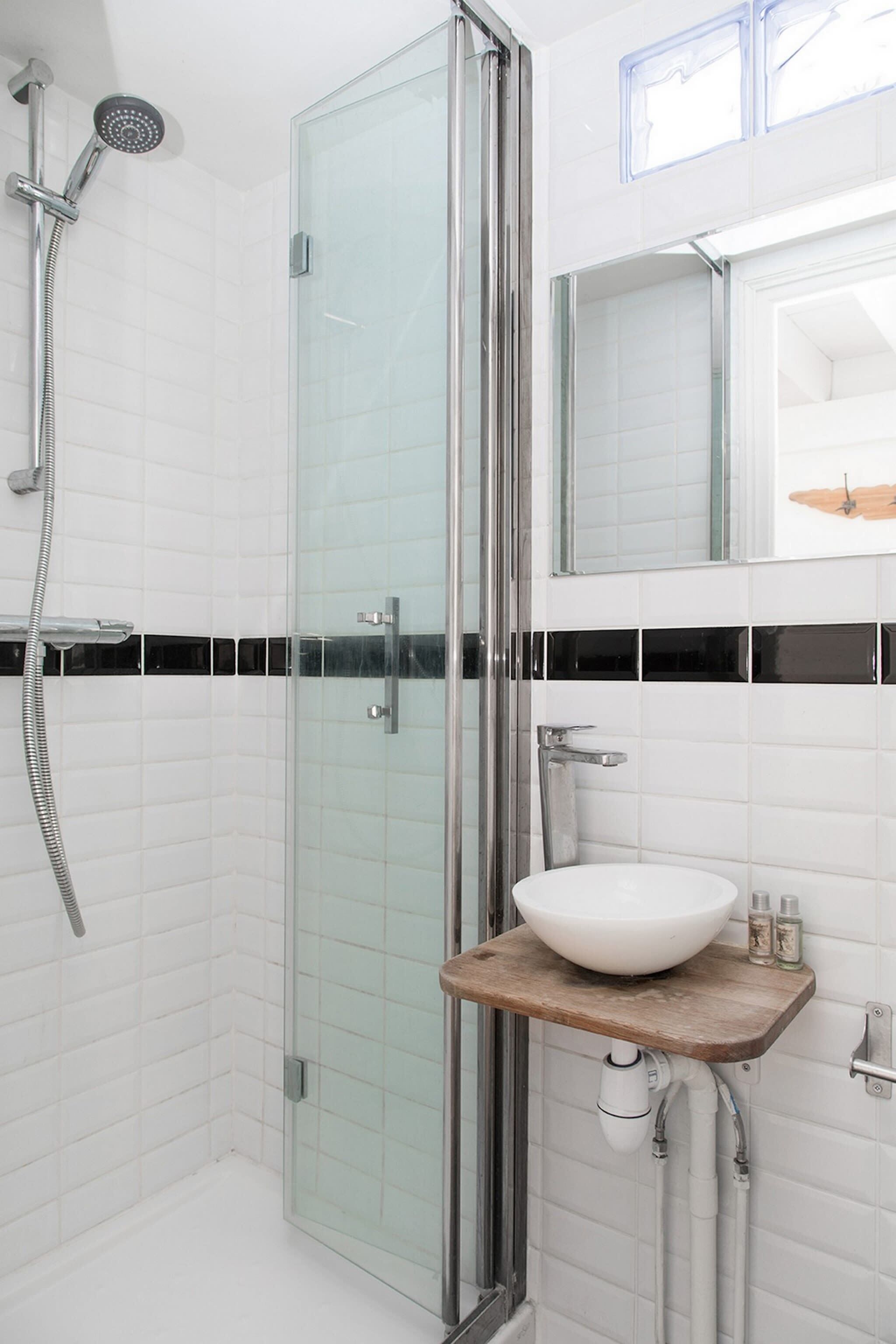 A modern bathroom with a glass shower enclosure, a white sink with a wooden countertop, and a mirror above the sink.