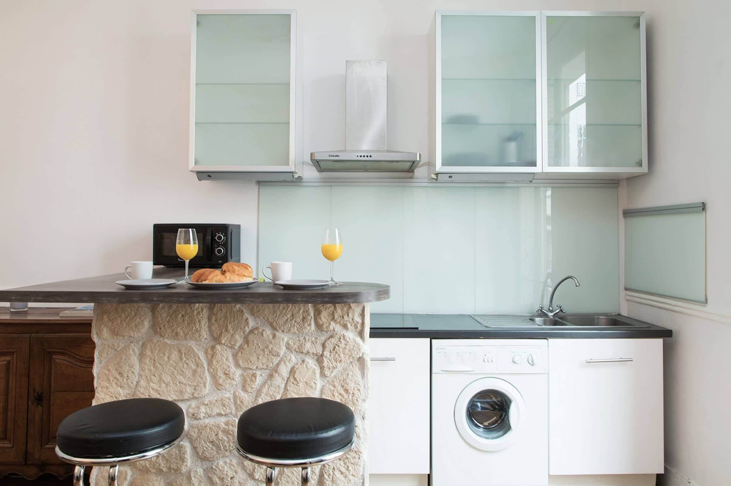 Una cucina compatta con isola in pietra, lavatrice e lavello.