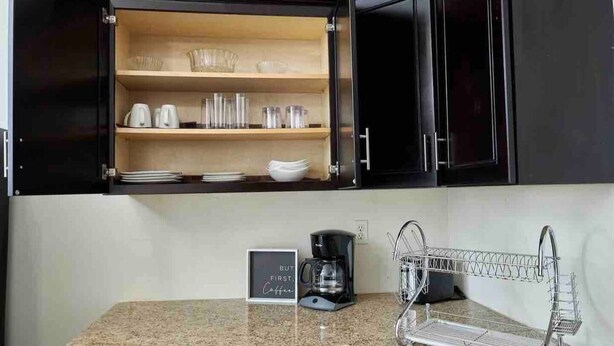 A kitchen with dark cabinets, a granite countertop, a coffee maker, and a dish rack. - Delva’s Place-Gated 3 bedroom - Pet Friendly (Freeport)