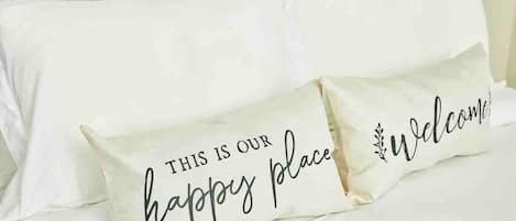 Two pillows on a bed with the text "THIS IS OUR happy place" and "Welcome" on them.