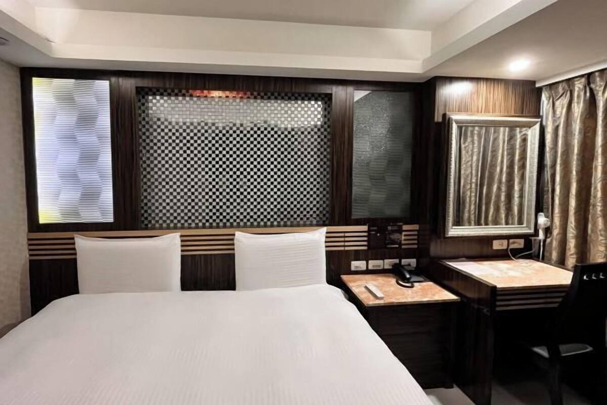 A hotel room with a bed, a desk, a chair, a telephone, and a window with curtains.