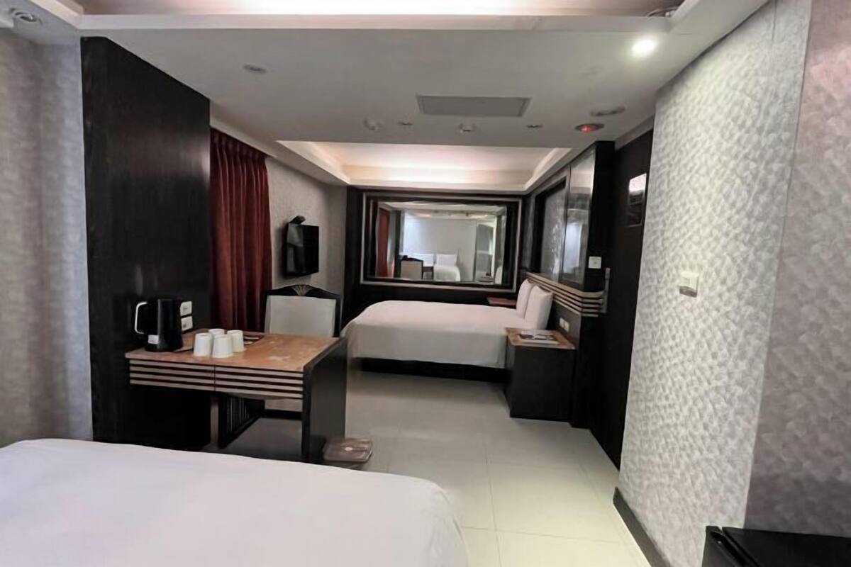 A hotel room with a bed, a desk with a coffee maker, a mirror, and a view of the hallway.