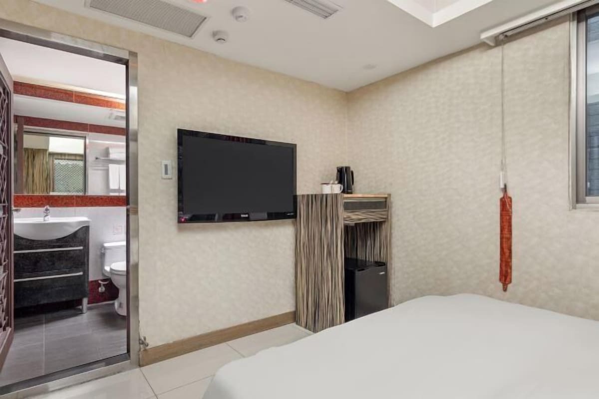A hotel room with a bed, a television, a bathroom with a sink and toilet, and a window.