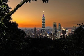 Paesaggio urbano con un grattacielo imponente, edifici densi e un tramonto.