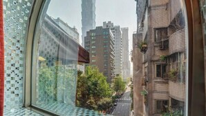 A view through a window with a mosaic pattern, featuring a tall building in the distance, likely a tower, and surrounding residential buildings. - Guide Hotel-Xinyi Branch（Ex HolyPro Hotel） (Taipei)