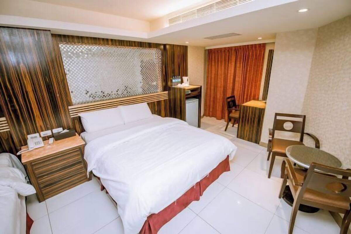 A hotel room with a bed, a desk, a chair, and a small table.