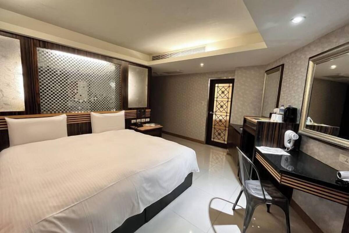A hotel room with a large bed, a desk with a mirror, and a vanity with a hairdryer.