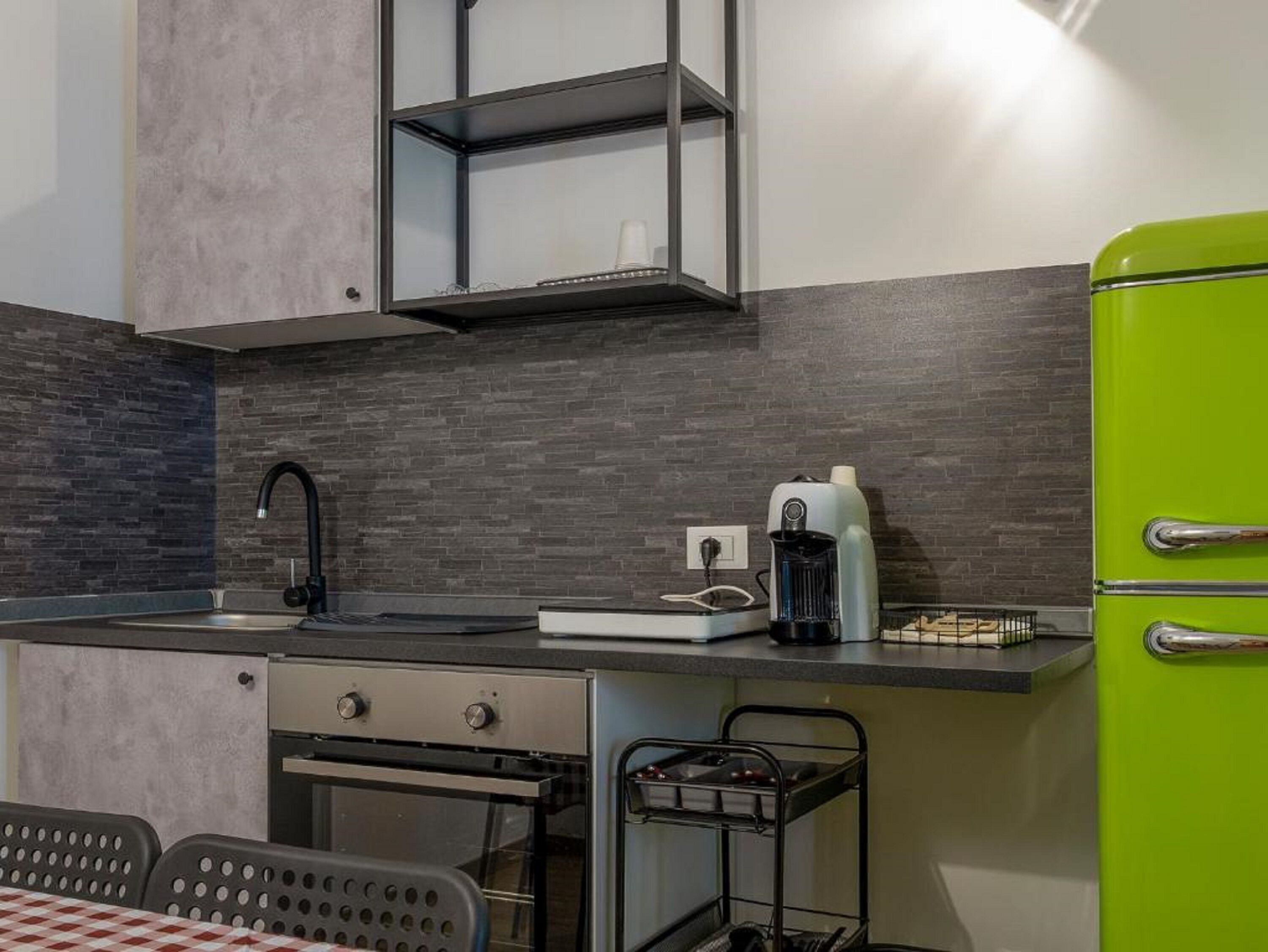 A kitchen with a modern design, featuring a grey brick backsplash, a black countertop, a green refrigerator, and a built-in oven.