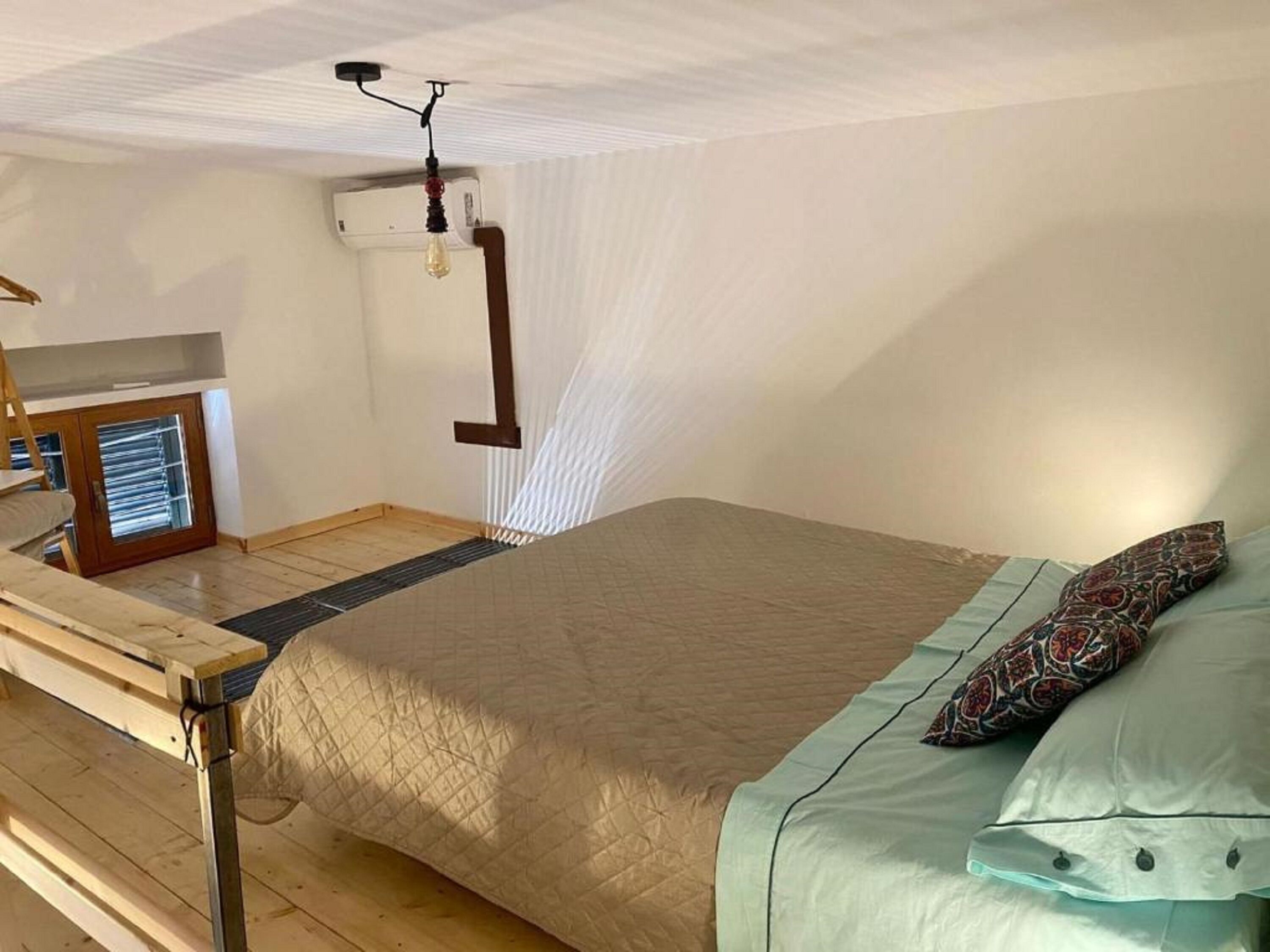A bedroom with a bed, a wooden bench, a radiator, and a window.