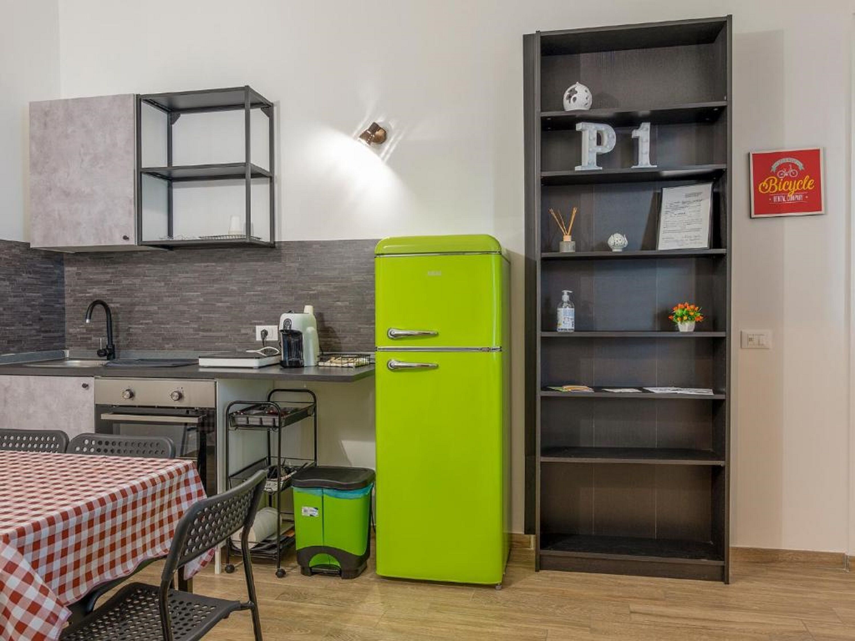 A compact kitchen with a green refrigerator, a small sink, and a dining area with a checkered tablecloth.