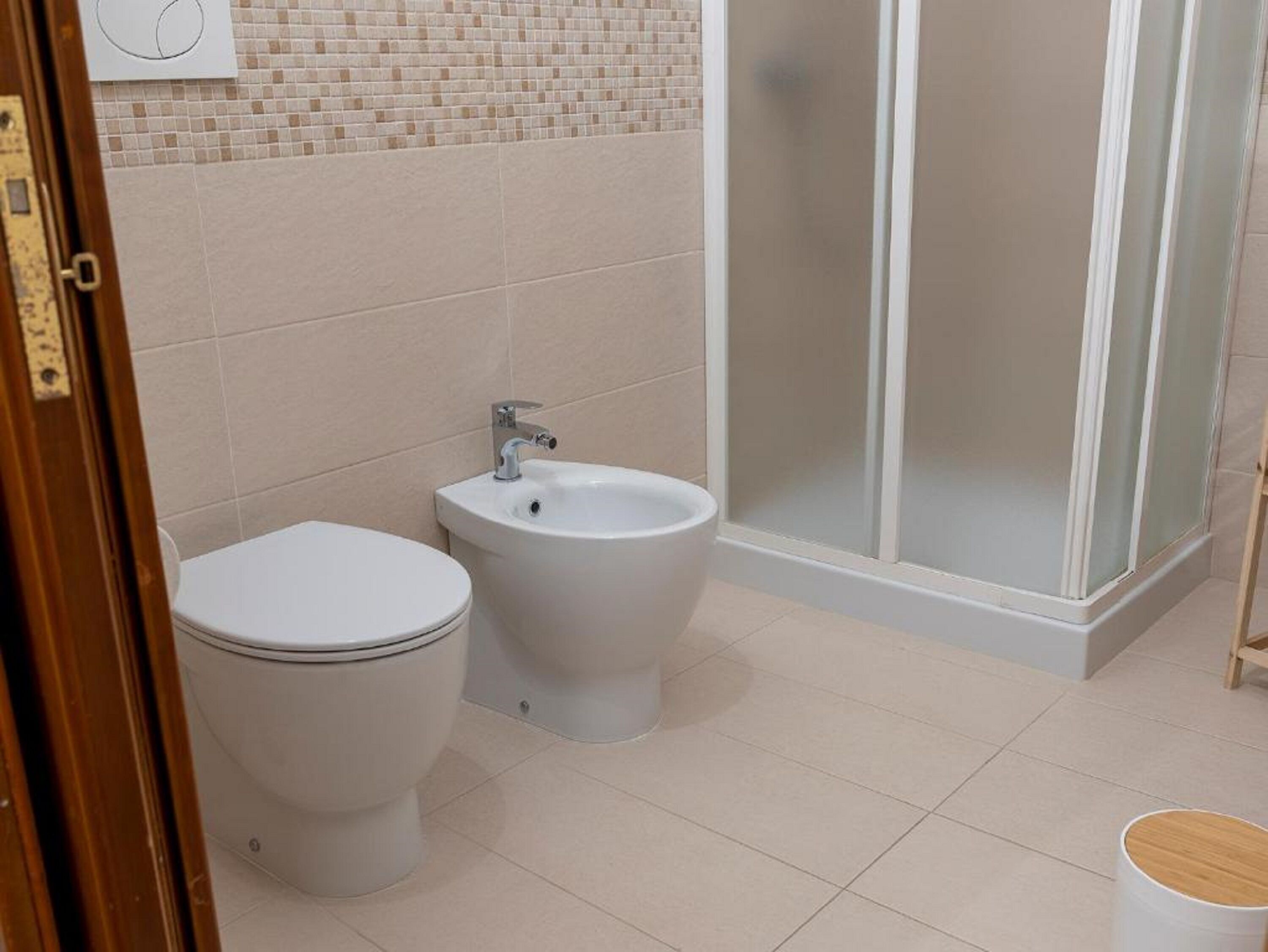 Baño con inodoro, bidé y ducha con mampara de vidrio.