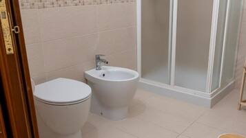 Baño con inodoro, bidé y ducha con mampara de vidrio.