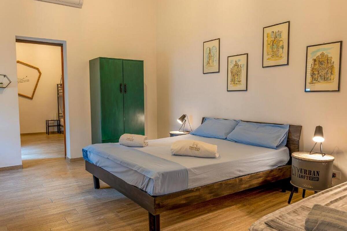 A bedroom with a wooden bed, a green wardrobe, and framed artwork on the wall.